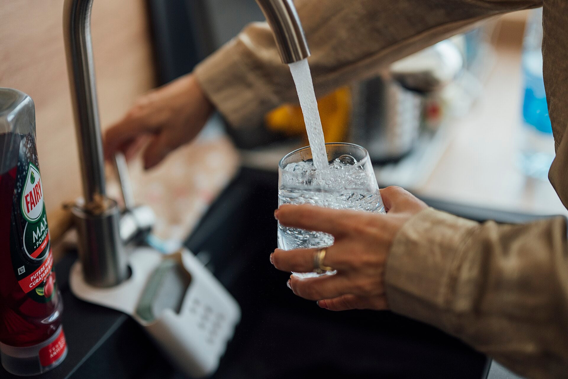 Person filling a glass with water from a kitchen faucet